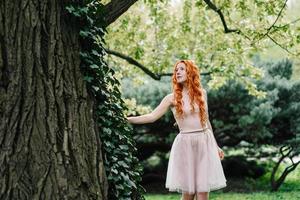 rothaariges junges Mädchen, das in einem Park zwischen Bäumen geht foto