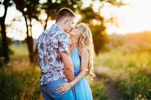 blondes Mädchen mit losen Haaren in einem hellblauen Kleid und einem Mann im Licht des Sonnenuntergangs foto