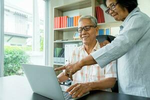 glücklich Senior asiatisch Paar mit ein Laptop beim Zuhause zum finden Neu Tourist Sehenswürdigkeiten zusammen. glücklich Pensionierung mit Planung, sparen, die Pension und das gut Hauptstadt Onkel von das Alten foto