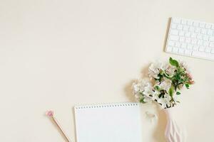 Arbeit von Zuhause Konzept eben legen auf Beige Tabelle mit Notizblock, Stift, Tastatur und Vase von Blumen. Aussicht von über. Kopieren Raum foto