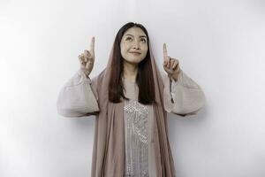aufgeregt asiatisch Muslim Frau tragen Kopftuch zeigen beim das Kopieren Raum über ihr, isoliert durch Weiß Hintergrund foto