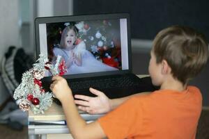 das Kind ist Sitzung beim ein Laptop und reden über Video Verknüpfung mit ein Freund. bleiben beim heim, Quarantäne und Sozial Distanzierung während das Neu Jahre. foto