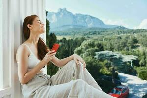 attraktiv jung Frau Sitzung auf das Balkon mit Telefon schön Berg Aussicht Sommer- Berg Aussicht foto