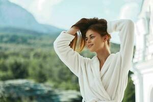 attraktiv jung Frau lange Haar im ein Weiß Bademantel bleiben auf das Balkon im ein Hotel Berg Aussicht foto
