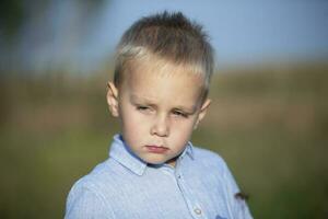 traurig wenig Junge mit blond Haar im ein Blau Shirt. foto