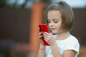 Kind mit ein Smartphone. das wenig Mädchen ist reden mit ein rot Telefon. foto