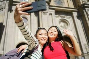 Erfreut asiatisch Frauen nehmen Selfie auf Smartphone lächelnd während Ausflug gegen Kathedrale von Granada foto