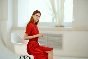 ziemlich Frau im rot Kleid Sitzung in der Nähe von das Fenster elegant Stil foto