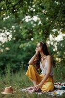 ein jung Hippie Frau meditiert im Natur im das Park, Sitzung im ein Lotus Position auf ihr bunt Plaid und genießen Harmonie mit das Welt im Öko-Kleidung im das Herbst foto