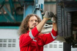 Auto Mechaniker Arbeiten im Garage, Techniker Mann Arbeiten im Auto Bedienung mit angehoben Fahrzeug, Auto Reparatur, und Instandhaltung foto