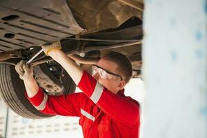 Auto Mechaniker Arbeiten im Garage, Techniker Mann Arbeiten im Auto Bedienung mit angehoben Fahrzeug, Auto Reparatur, und Instandhaltung foto