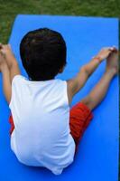 asiatisch Clever Kind tun Yoga Pose im das Gesellschaft Park draussen, Kinder- Yoga Pose. das wenig Junge tun Yoga und Meditation Übung. foto