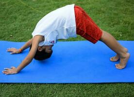 asiatisch Clever Kind tun Yoga Pose im das Gesellschaft Park draussen, Kinder- Yoga Pose. das wenig Junge tun Yoga und Meditation Übung. foto