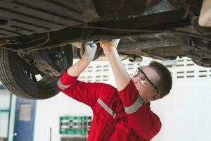 Auto Mechaniker Arbeiten im Garage, Techniker Mann Arbeiten im Auto Bedienung mit angehoben Fahrzeug, Auto Reparatur, und Instandhaltung foto