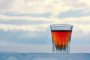 ein schön Glas von Alkohol steht auf ein eisig Base gegen das Himmel. gekühlt Whiskey draußen im Winter. Orange trinken im ein Glas. Kopieren Raum. Seite Sicht. horizontal. foto