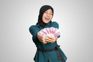 Porträt von aufgeregt asiatisch Hijab Frau im beiläufig Outfit zeigen einer hundert tausend Rupiah. finanziell und Ersparnisse Konzept. isoliert Bild auf Weiß Hintergrund foto