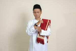 Porträt von attraktiv asiatisch Muslim Mann im Weiß Hemd suchen auf Handgelenk Uhr realisieren Das er ist bekommen spät zum ein treffen. isoliert Bild auf grau Hintergrund foto