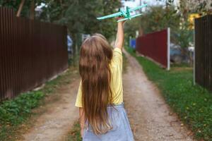 glückliches Kindermädchen mit langen blonden Haaren, das bei Sonnenuntergang mit Spielzeugflugzeug im Freien spielt foto