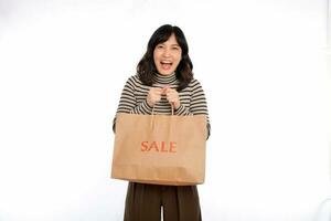 glücklich jung asiatisch Frau beiläufig Uniform halten Einkaufen Papier Tasche isoliert auf Weiß Hintergrund. Einkaufen Rabatt Konzept foto