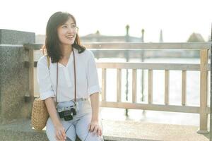 jung schön asiatisch Frau Reisender Sitzung durch das Fluss beim sonnig Tag foto