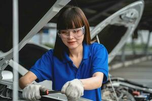 glücklich asiatisch Frau Auto Mechaniker im Garage. Fachmann Auto Mechaniker Wer inspiziert und Instandsetzung Motor im Garage. Auto Reparatur und Instandhaltung Konzept. suchen beim Kamera foto