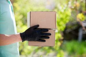 Lieferung Mann halten Karton Kisten im medizinisch Gummi Handschuhe beim Sonnenuntergang auf draussen. foto