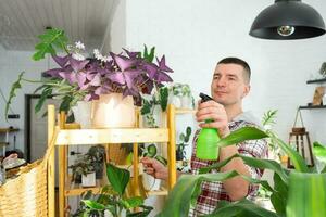 Mann Sprays von ein sprühen Gewehr Zuhause Pflanzen von ihr Sammlung, gewachsen mit Liebe auf Regale im das Innere von das Haus. Zuhause Pflanze wachsend, Grün Haus, Wasser Gleichgewicht, Befeuchtung foto