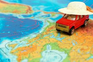 Spielzeug Auto im ein Stroh Hut auf das physisch Karte von das Welt, Reise Inhalt foto