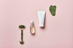 kosmetisch Schönheit Produkte und Stein Massagegeräte auf Rosa Hintergrund. Gesicht Massage Hautpflege Konzept foto