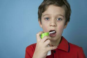 kaukasisch Junge Sprays ein Aerosol in seine Mund zu behandeln wund Kehle, sprühen zum aktuell verwenden. Aerosol Inhalator foto