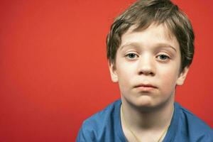 Porträt von ein traurig kaukasisch Junge von Vorschule Alter auf ein rot Hintergrund foto