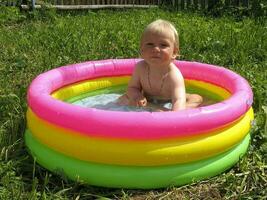 Kind ist Sitzung im ein bunt aufblasbar Schwimmbad mit Wasser im Sommer- foto