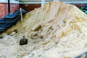 ein Stapel von Gelb Fluss Sand mit ein Schaufel auf ein Konstruktion Seite? ˅ foto