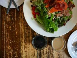 Salat mit Lachs, Speck, Gemüse ein Dressing auf ein hölzern Tabelle foto