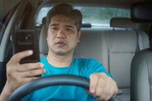 asiatisch Mann mit Handy, Mobiltelefon Clever Telefon und lesen Mitteilungen während Fahren ein Wagen. Konzept von Fahrlässigkeit, gefährlich Verhalten und Unfall Risiko foto