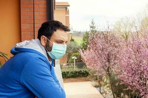 jung kaukasisch Mann mit Maske suchen aus auf zu Zuhause Terrasse während Quarantäne fällig zu Coronavirus covid19 Pandemie. foto