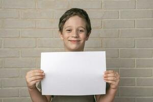 ein heiter lächelnd 5 Jahre alt europäisch Junge hält ein leeren Poster über seine Kopf foto