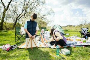 glücklich jung Familie, Mutter und Kinder haben Spaß und genießen draussen auf Picknick Decke Gemälde beim Garten Frühling Park, Entspannung. foto