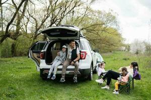 Familie mit drei Kinder gegen Auto öffnen Kofferraum auf Picknick. foto