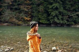 Frau im ein Gelb Jacke in der Nähe von das Fluss Berge Natur gehen foto