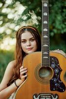 jung Hippie Frau mit Öko Bild lächelnd und suchen in das Kamera mit Gitarre im Hand im Natur auf ein Ausflug foto