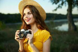 ziemlich Frau mit ein Kamera im ihr Hände auf Natur tragen Hut rot Lippen Lächeln sieht aus oben foto
