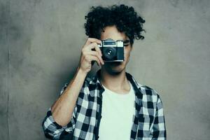 Fotograf im ein Plaid Hemd mit ein Kamera im seine Hand auf ein grau Hintergrund im ein Hobby Studio Zimmer foto