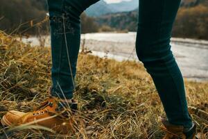 Damen Füße Jeans Schuhe trocken Gras Herbst Fluss Berge im das Entfernung foto