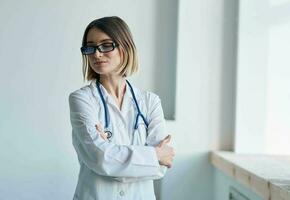 Arzt Frau im ein medizinisch Kleid mit ein Stethoskop im Brille sieht aus aus das Fenster foto