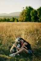 Frau Sitzung im Feld mit Dackel Hund lächelnd während Ausgaben Zeit im Natur mit Freund Hund im Herbst beim Sonnenuntergang während Reisen foto