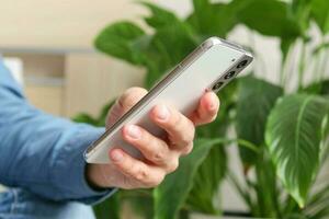 schließen oben Bild von männlich Hände mit Smartphone im Zuhause Innere, Suche oder Sozial Medien Konzept, Mann Tippen SMS Botschaft zu seine freunde foto