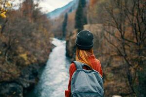 Frau mit Rucksack im Natur auf das Brücke in der Nähe von das Fluss Berge Abenteuer foto