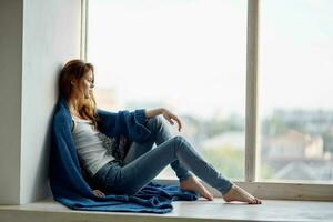 schön Frau Sitzung in der Nähe von das Fenster mit ein Blau Plaid sich ausruhen foto