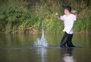 asiatisch Junge im Weiß T-Shirt ist Ausgaben seine Freizeit durch Tauchen, Baden, werfen Felsen und fangen Fisch im das Fluss glücklich, Hobby und Glück von Kinder Konzept, im Bewegung. foto